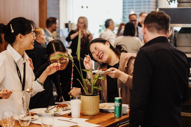 People laughing and enjoying food together at DL25-M, gathered around a table with plates and drinks.