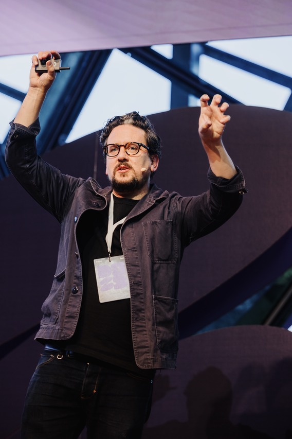 Ben Keenan presenting on stage at DO23: Rediscover Creativity, engaging the audience with an animated gesture.